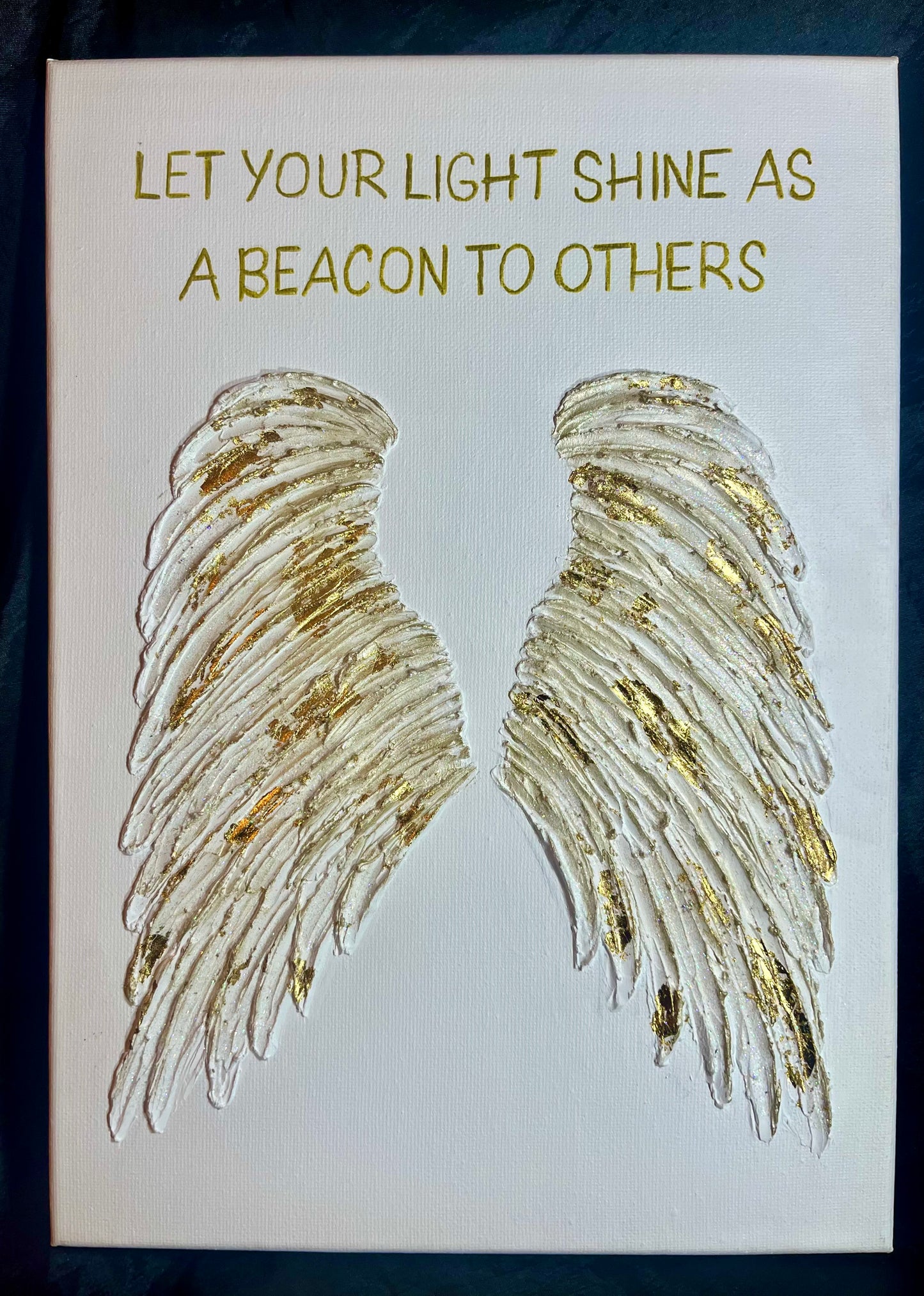Decorative canvas with gold angel wings and motivational quote on a white background
