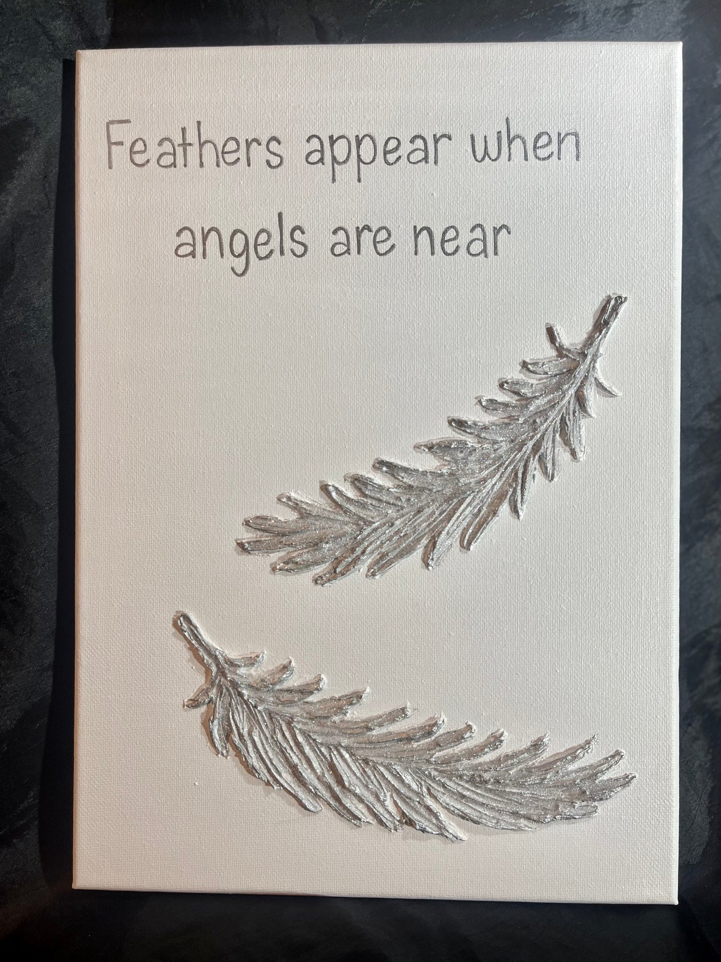 Canvas with silver feathers and text 'Feathers appear when angels are near' on a white background