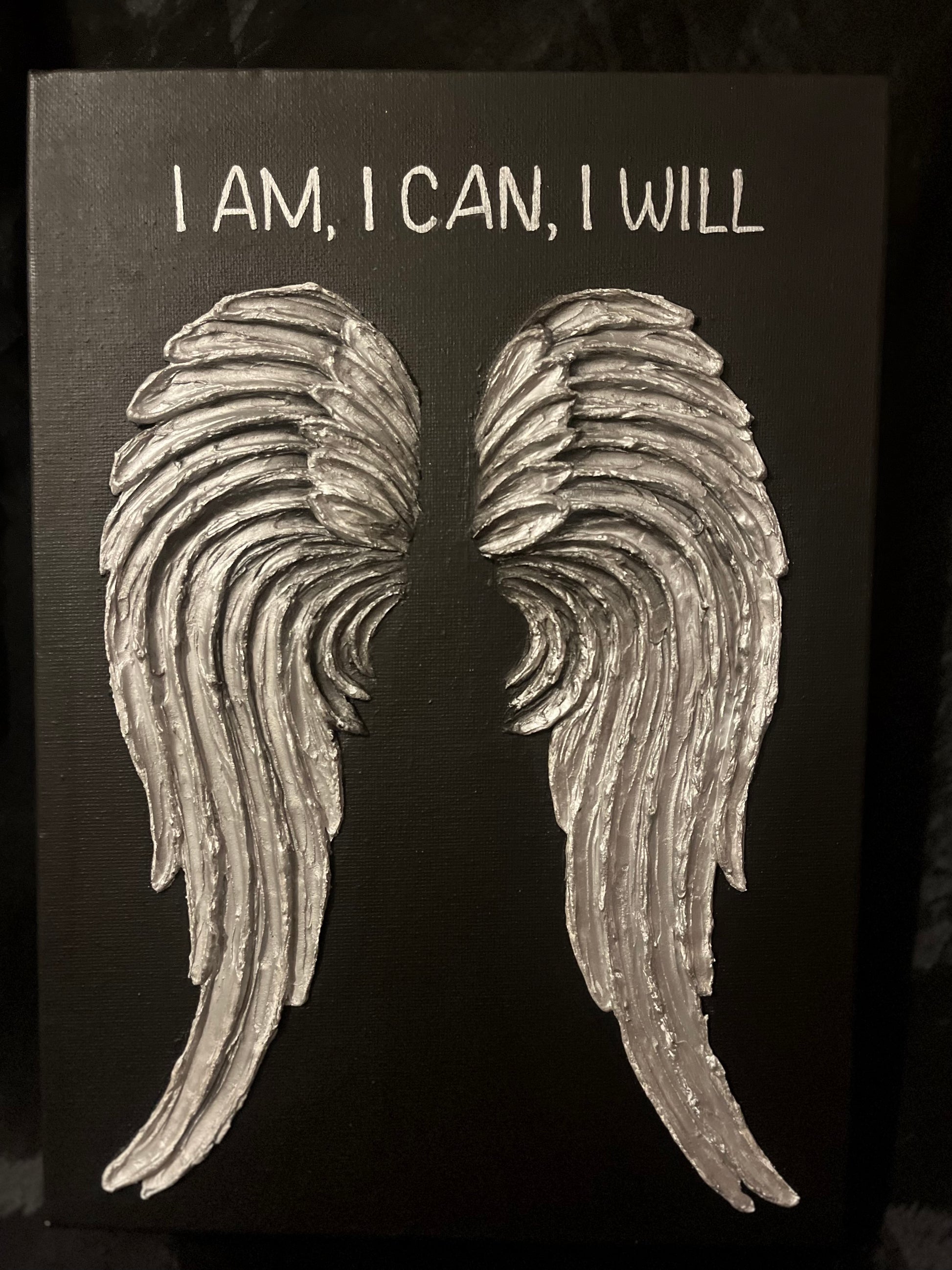 Decorative wall art with angel wings and motivational text on a black background